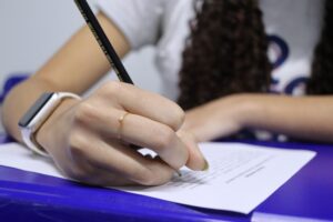 mão de uma menina em primeiro plano escrevendo em uma folha